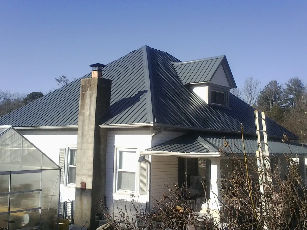 Dark blue standing seam metal roof on a white farmhouse with dormer — Slate & Tile Roof Repair by Roofing Brothers in Millers Creek
