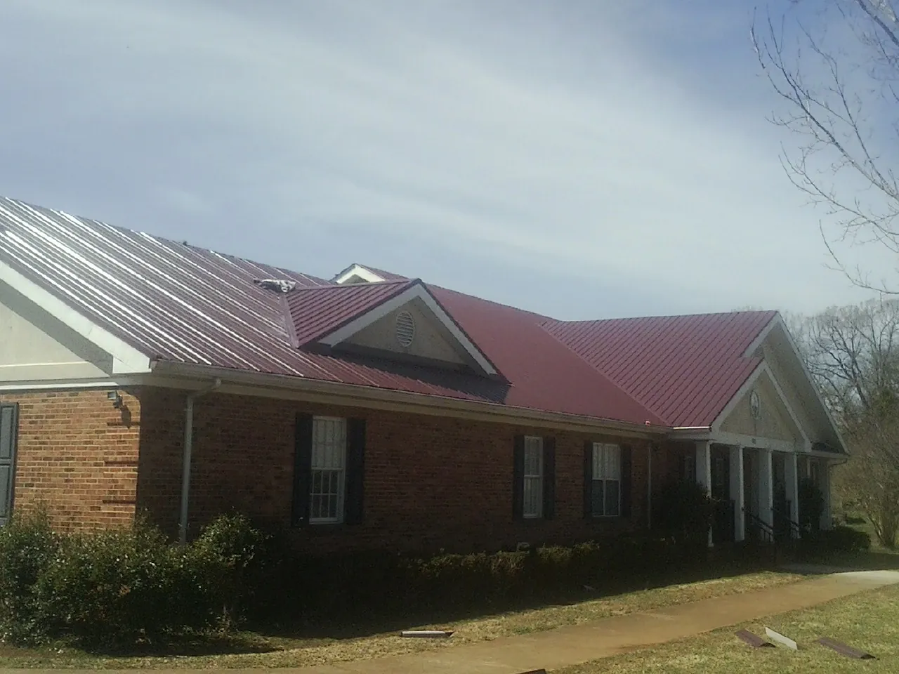 Red metal roof with gabled entries on a long brick building, from a Hail Damage Roof Repair job in Millers Creek