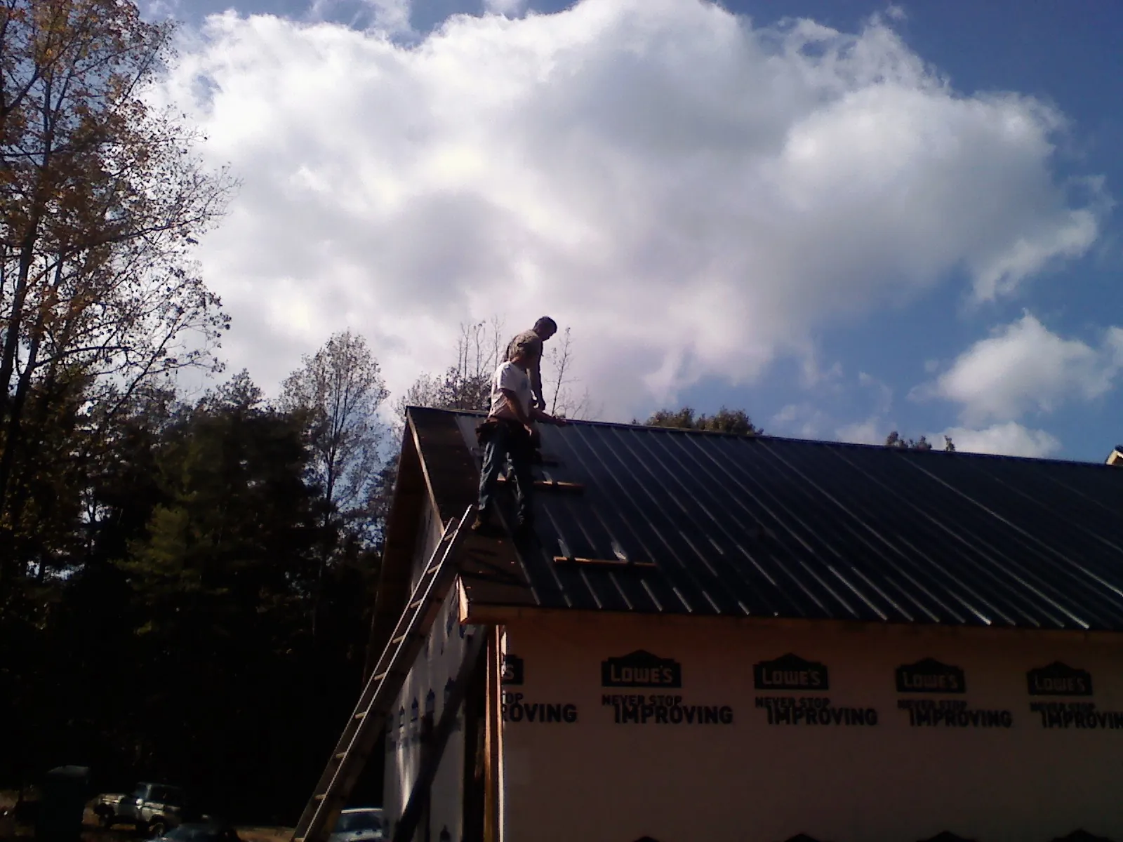 Roofer fastening dark metal panels high against a cloudy sky, from a Roof Inspection job in Millers Creek