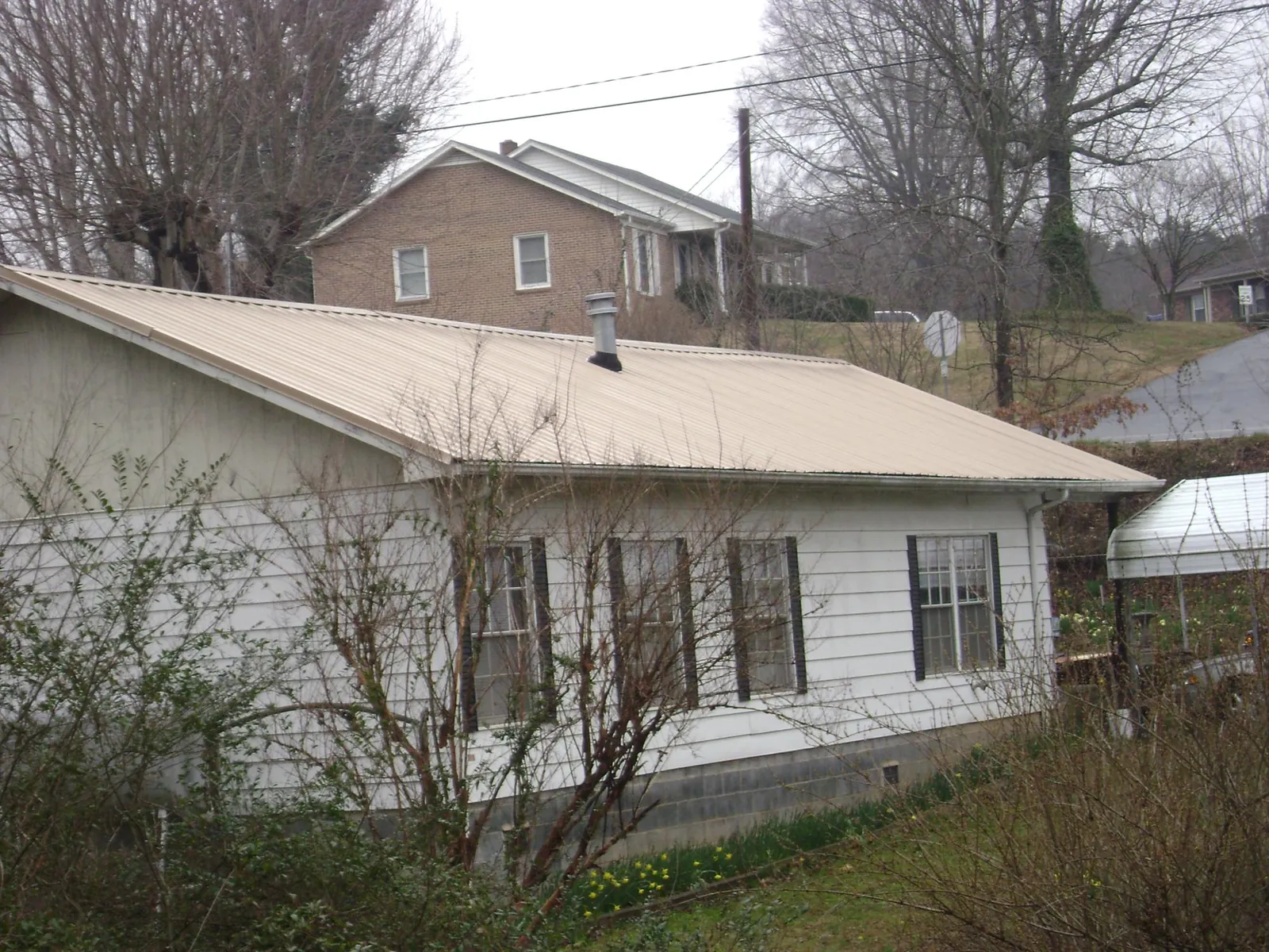 Tan metal roof on a white sided house set into a hillside — Commercial Roofing by Roofing Brothers in Millers Creek