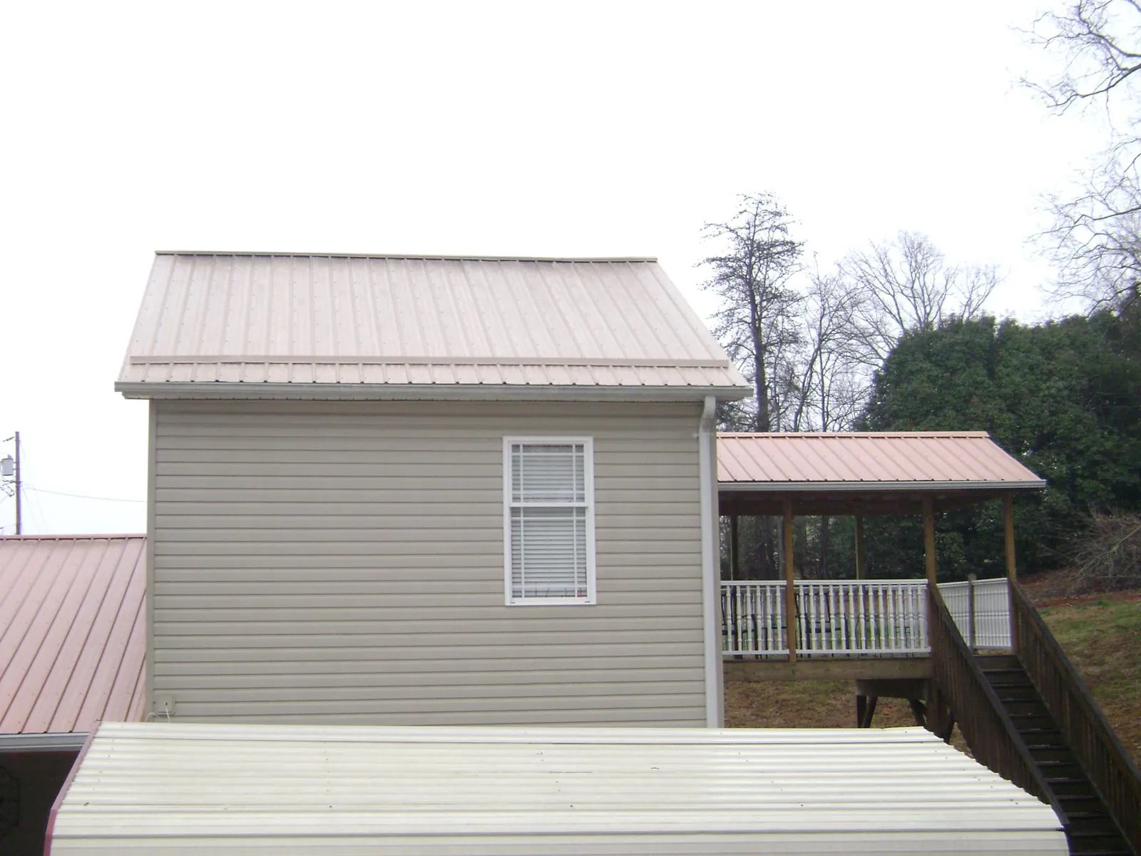 Tan metal roofs on a two story addition and attached porch, from a Roof Replacement job in Millers Creek